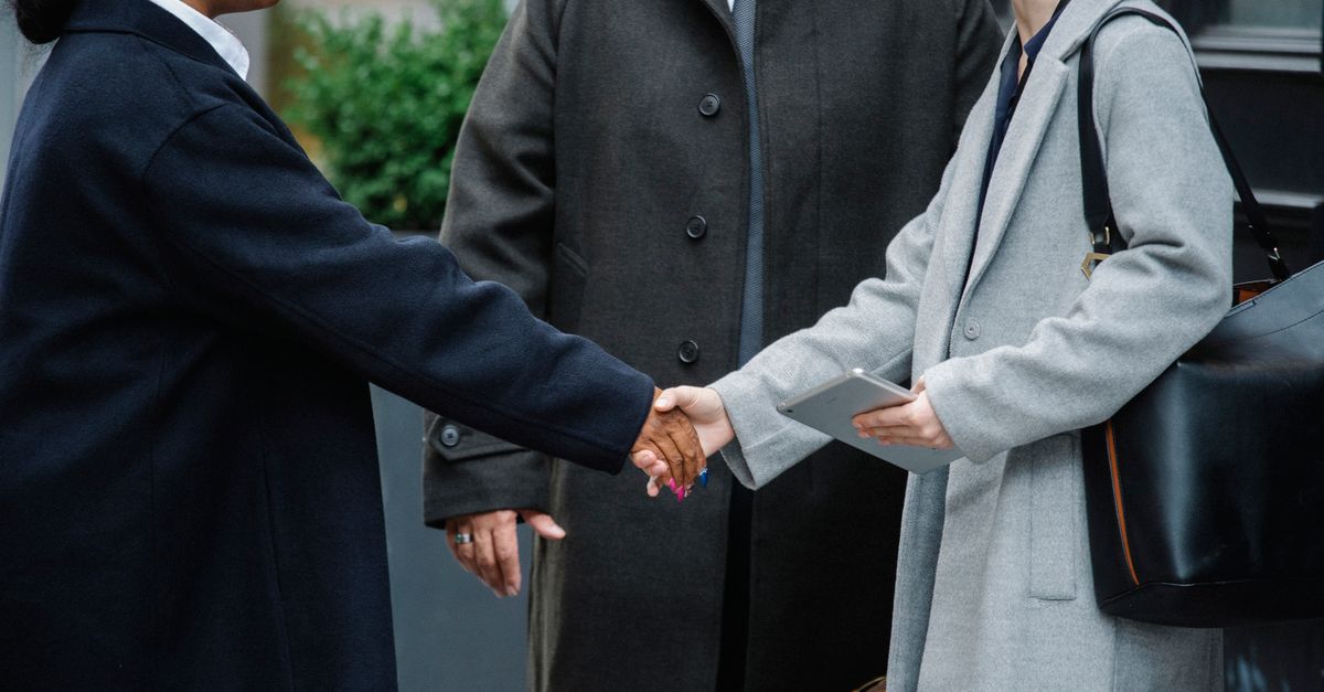Doctor in white coat and hospital manager in business attire shaking hands in a hospital corridor