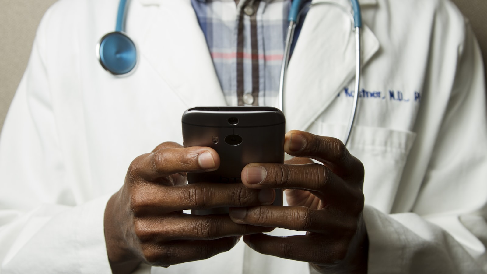 Médica olhando o smartphone com a agenda de consultas aberta sobre uma mesa de consultório