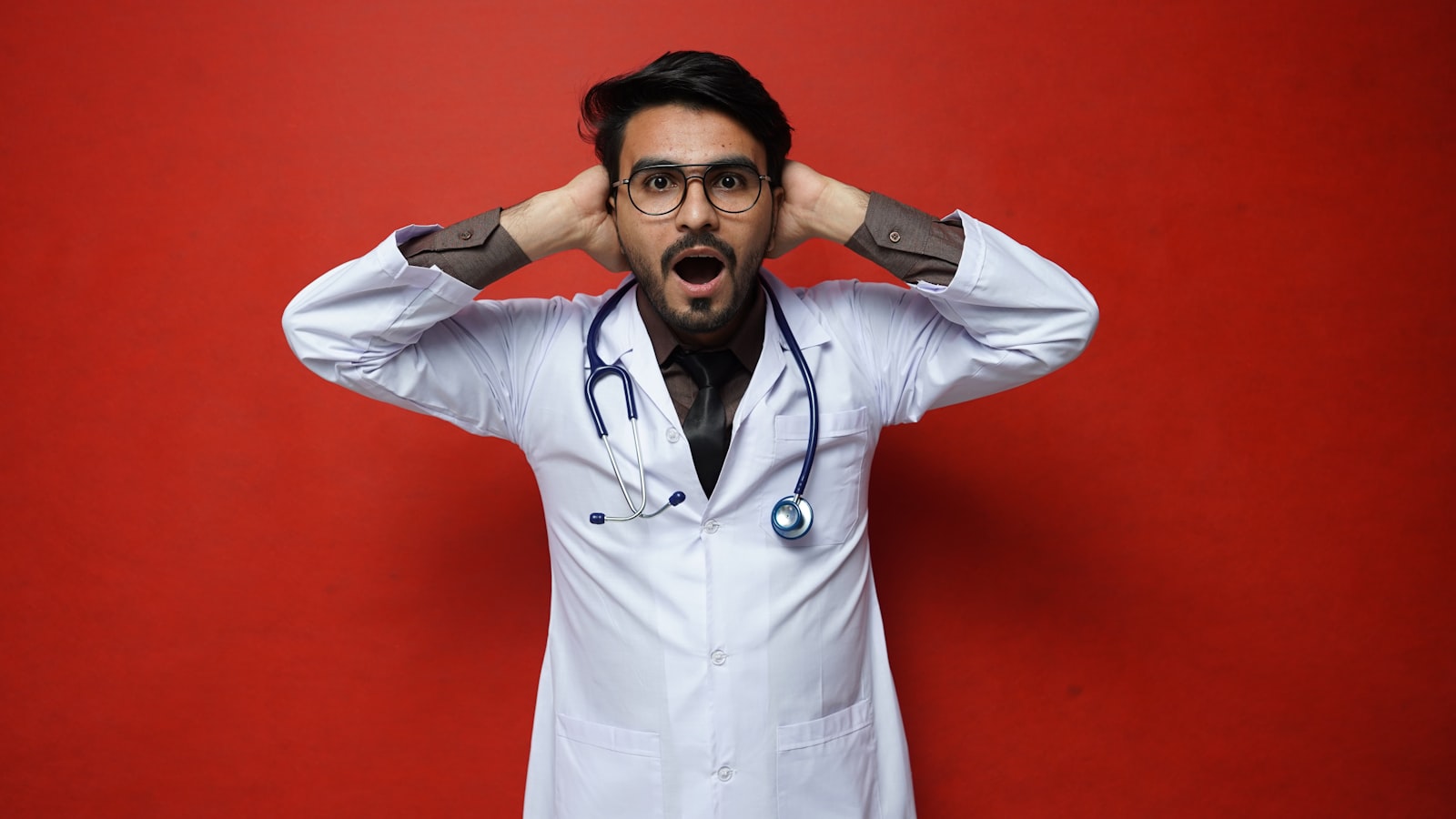 Médico de jaleco branco com expressão de exaustão em corredor hospitalar