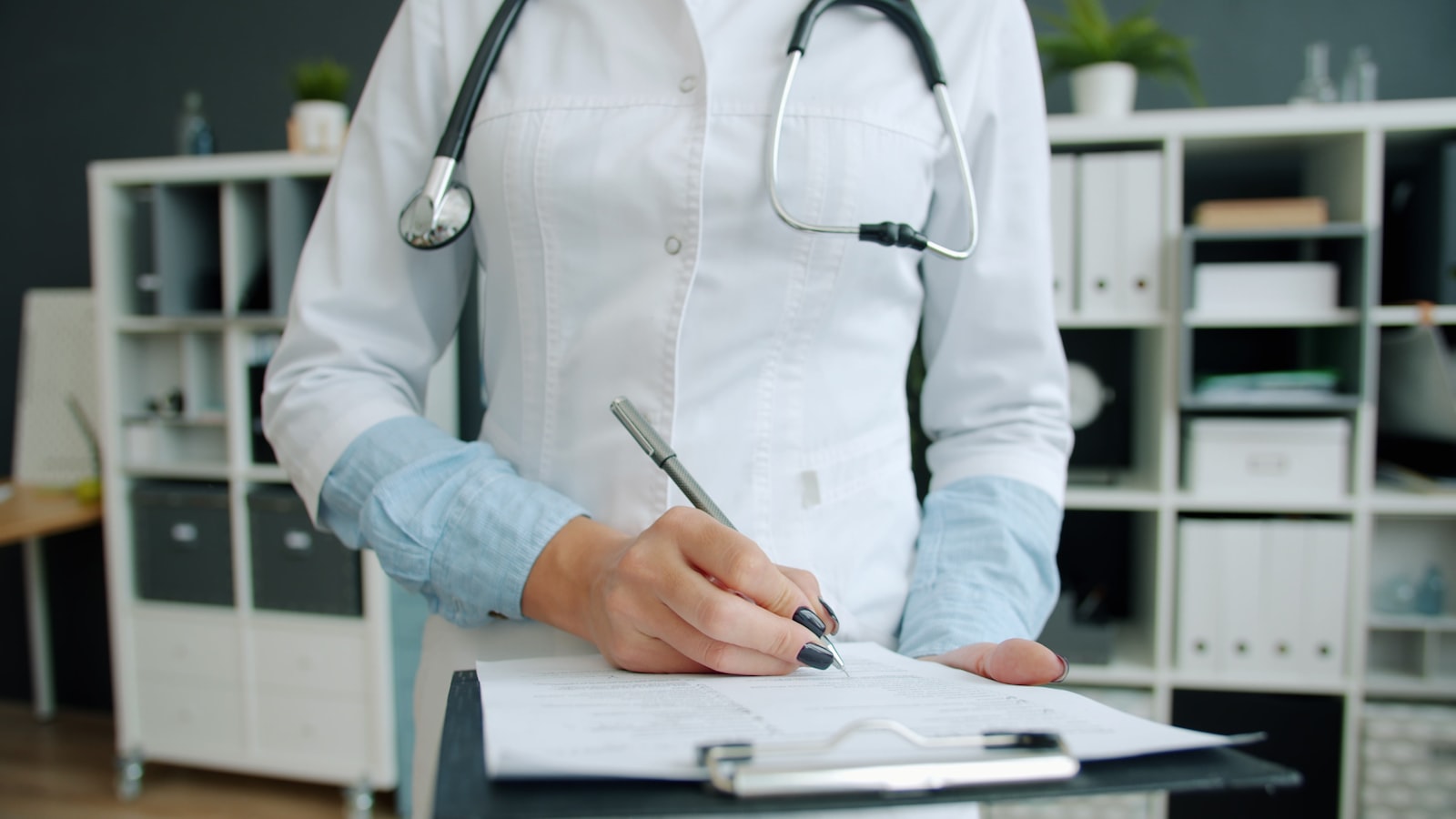Médica em jaleco branco preenchendo documento em consultório moderno