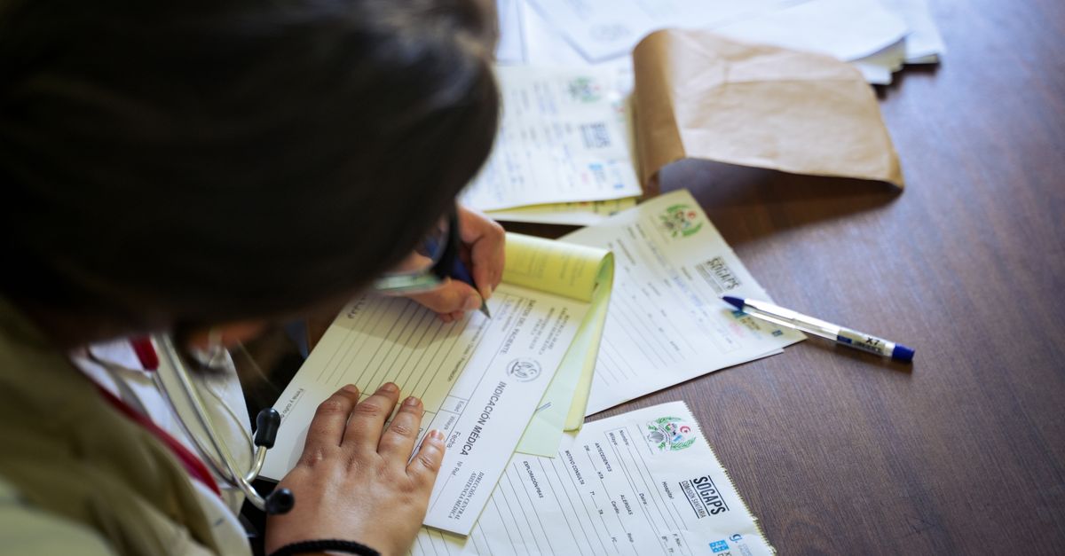 Mesa de consultório médico com documentos financeiros, calculadora e caneta