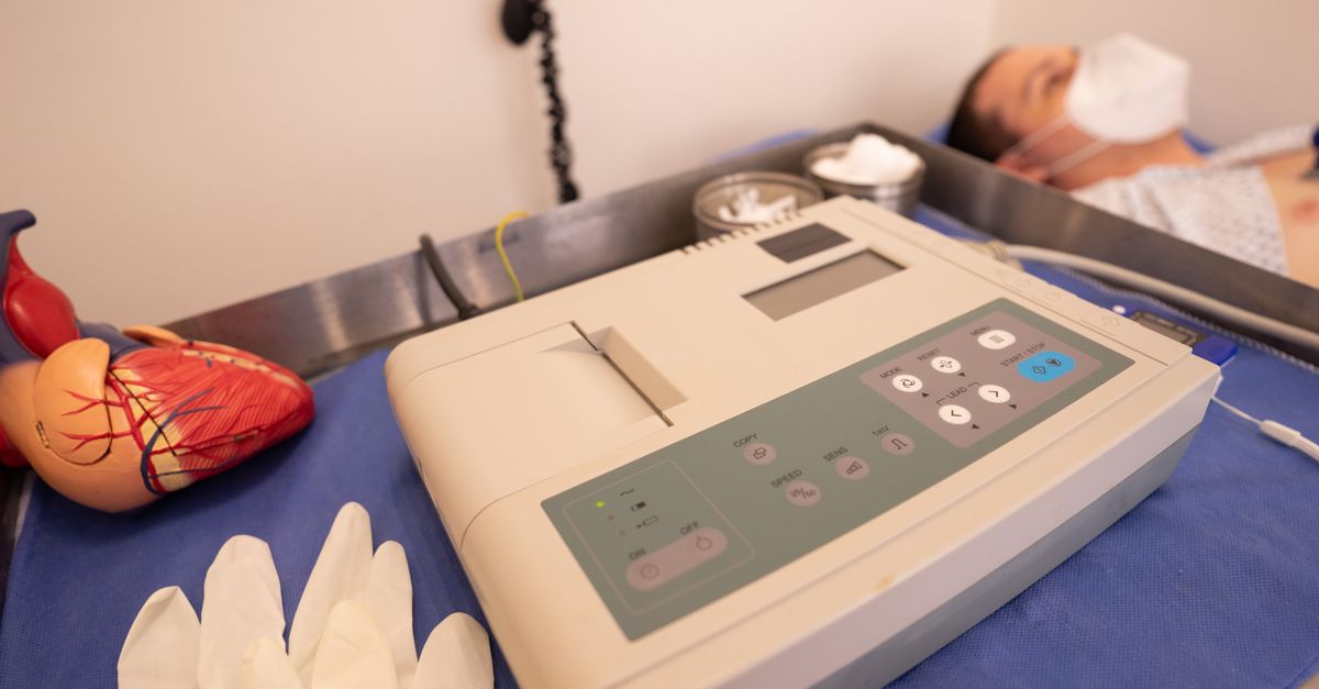 Eletrocardiógrafo e modelo anatômico de coração ao lado de paciente deitado em maca