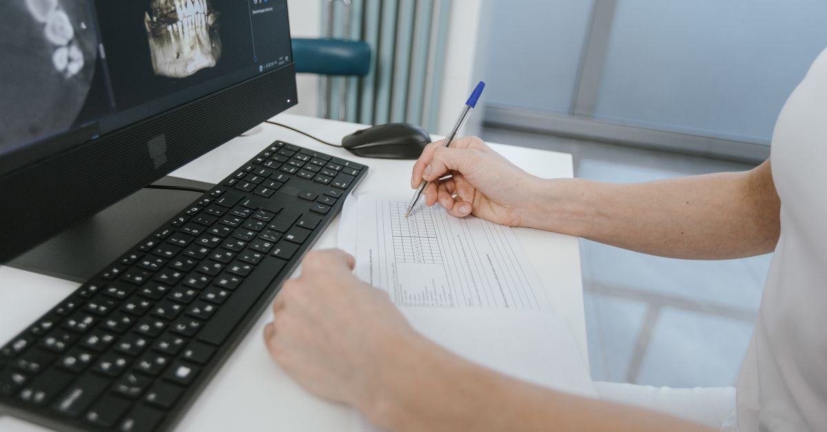 médico conferindo documentos financeiros e nota fiscal no laptop em consultório