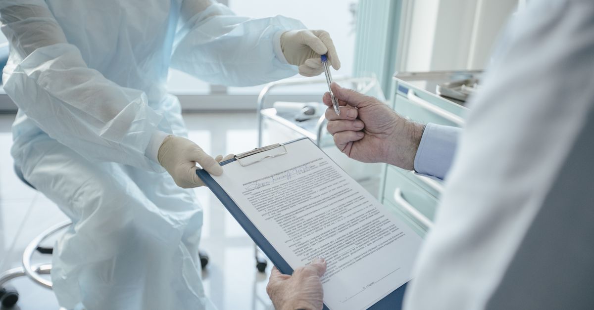 Doctor reviewing medical consent paperwork at desk with laptop and medical documents